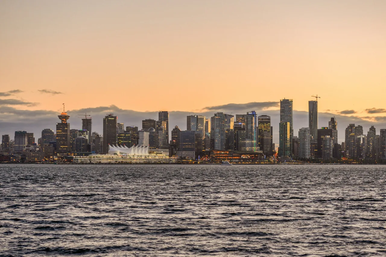 The Vancouver skyline and its white sail-roofed waterfront building glowing at sunset, seen across the water